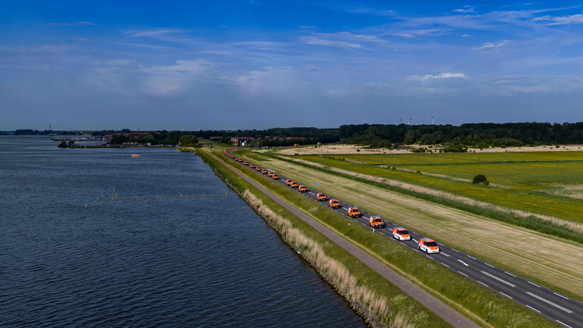 Stoet van oranje KSN bussen aan de Harderdijk, vlakbij Biddinghuizen